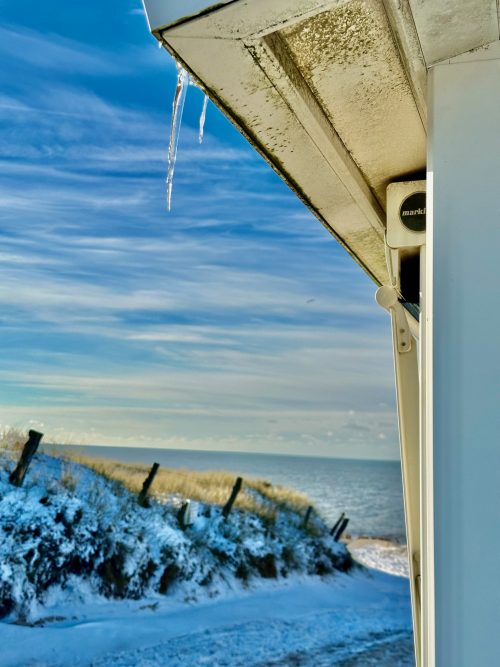 Winter auf Sylt Kampen Kartenhäuschen mit Eiszapfen und Strand im Hintergrund und strahlend blauem Himmel